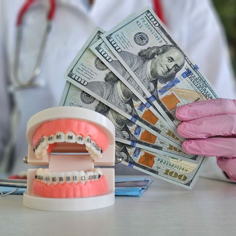 Gloved hand holding money next to braces model